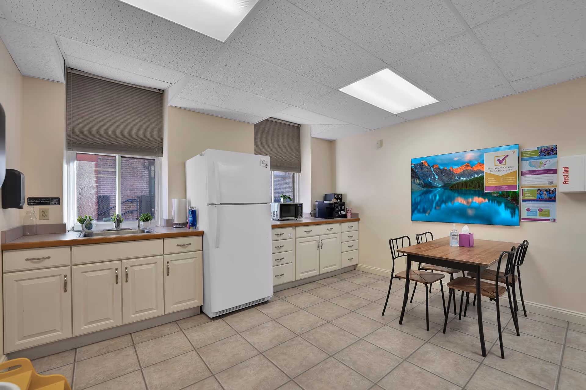 Bright kitchenette with cabinet counters, a refrigerator, and a small dining table in a residential facility