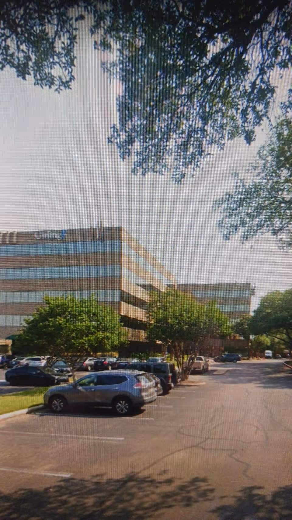 Exterior view of a multi-story office building with a parking lot and surrounding trees.