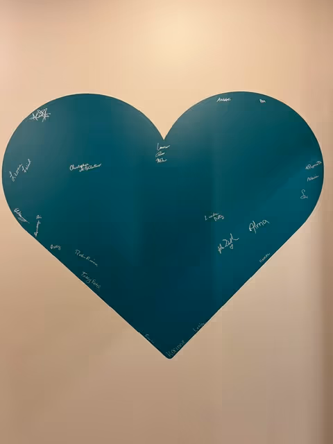 A large teal heart mural on a white wall, covered with signatures.