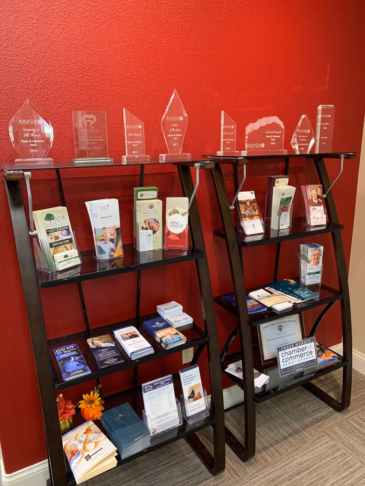 Two black brochure stands with pamphlets and glass awards against a red lobby wall.