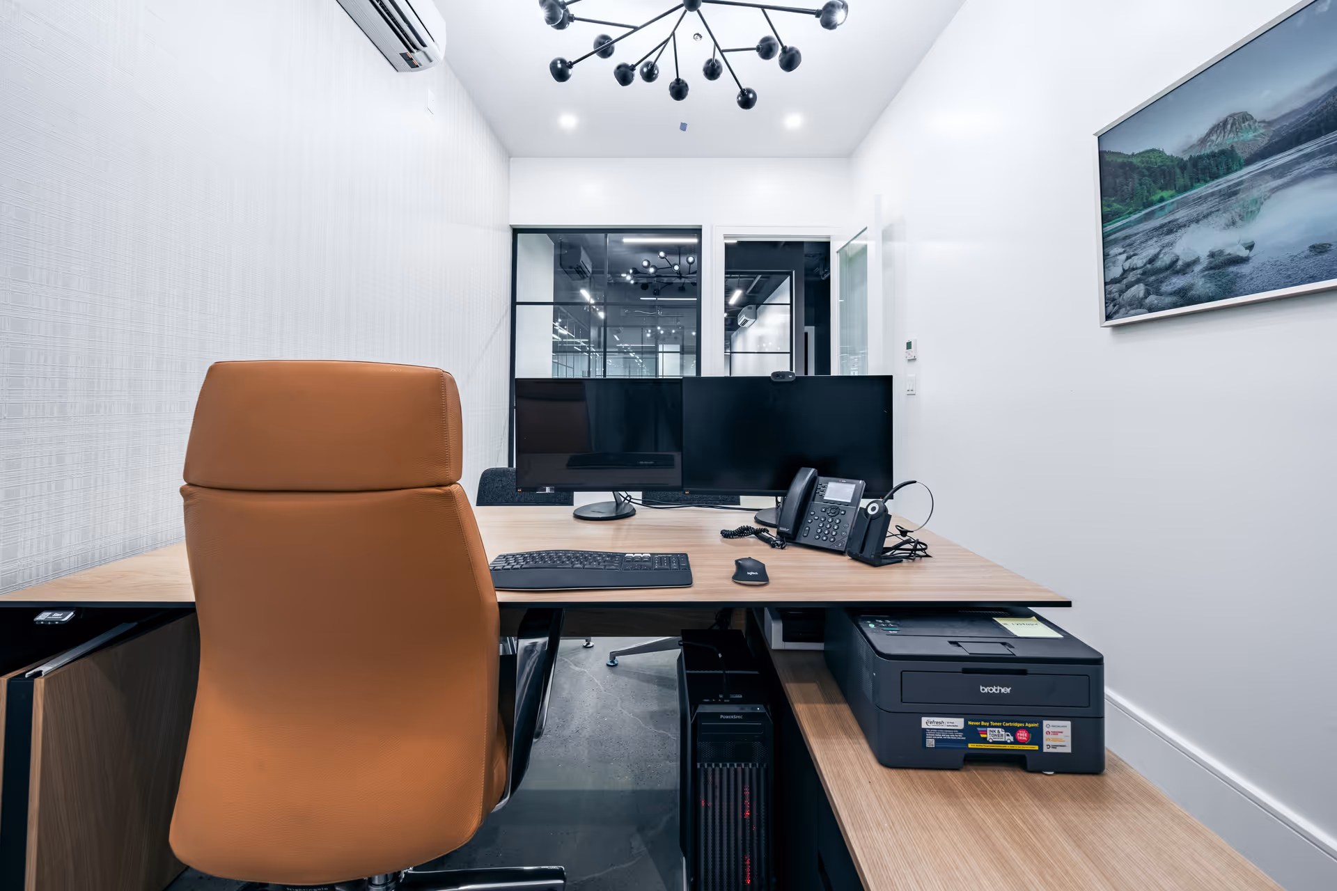 Modern office desk with dual monitors, phone, keyboard, and brown leather chair.