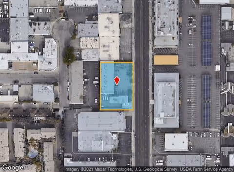 Aerial view of city block highlighting blue-roofed building outlined in yellow with a red pin.