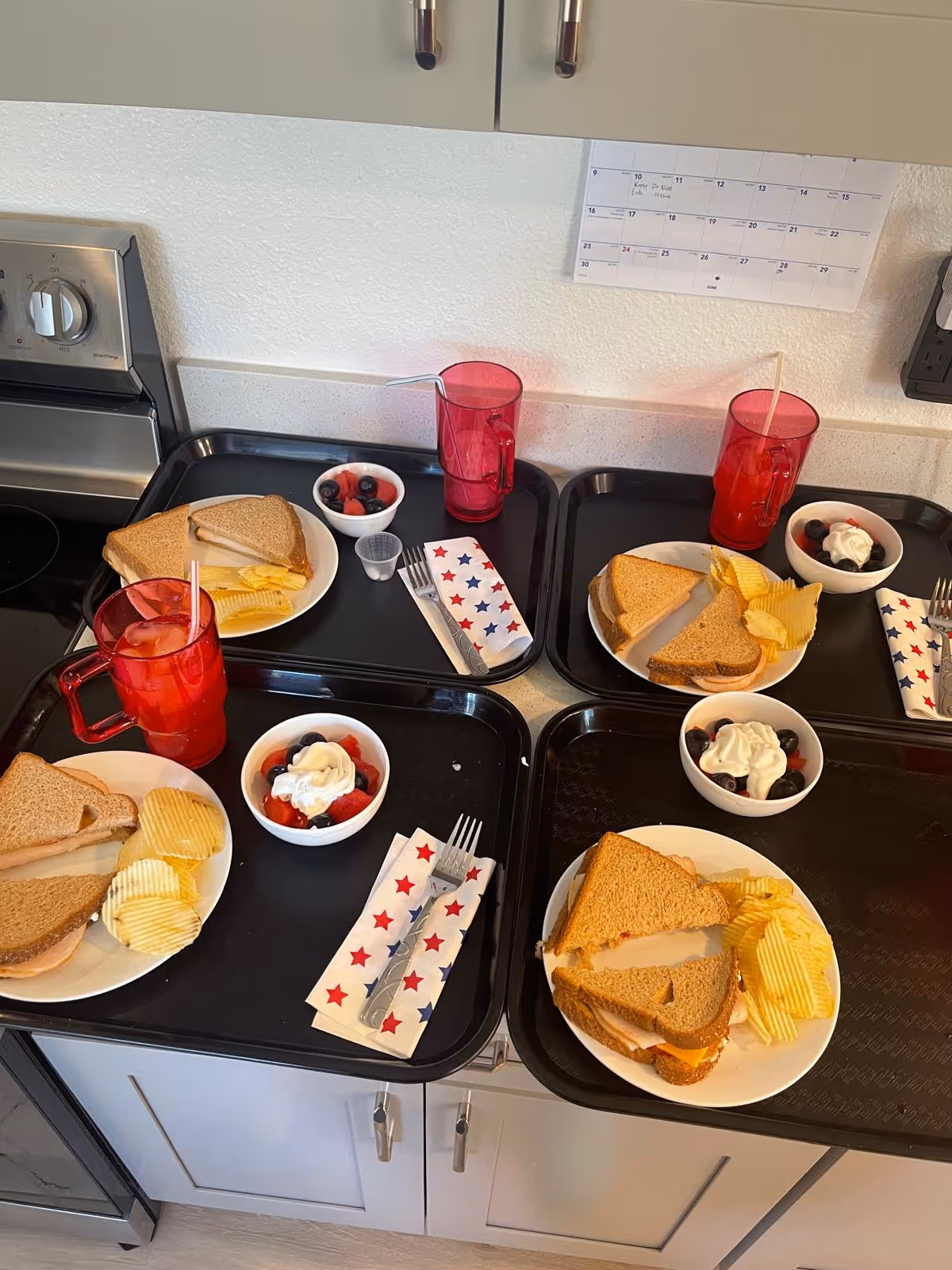 Meal trays with sandwiches, berries, chips, and whipped cream on a kitchen counter.
