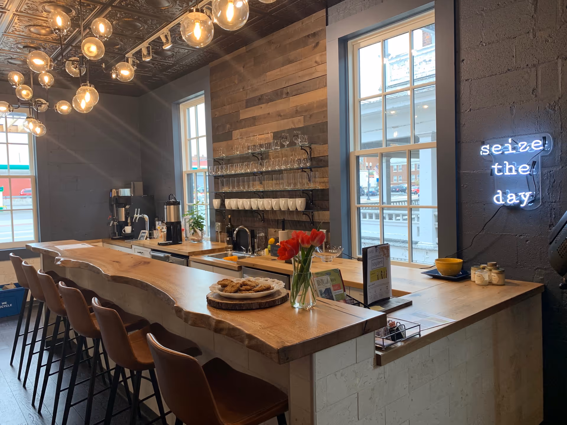 Interior view of a modern cafe-style kitchen with a wooden island, stools, and coffee setup.