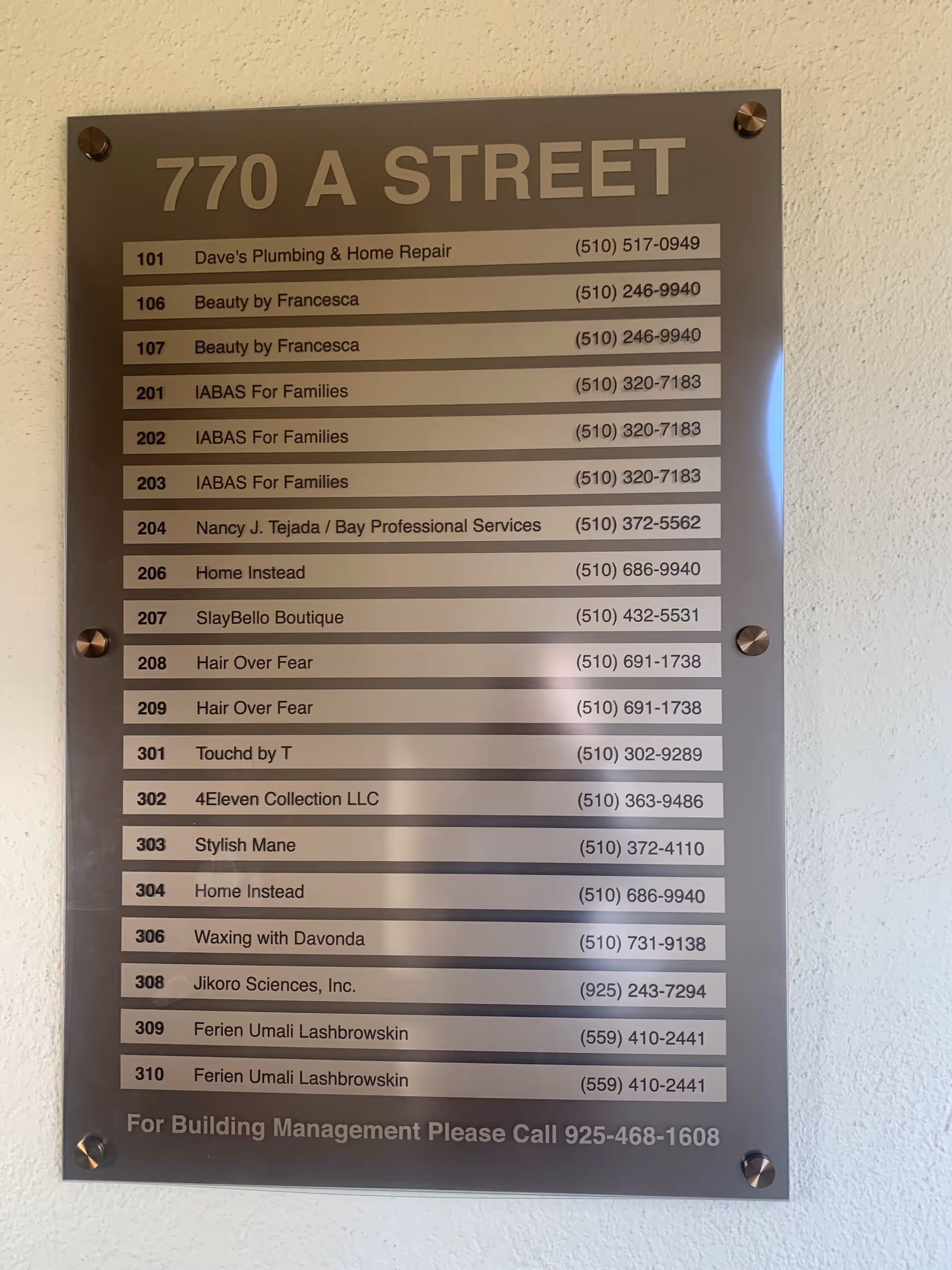 Metal directory plaque listing units, names, and phone numbers mounted on a wall.
