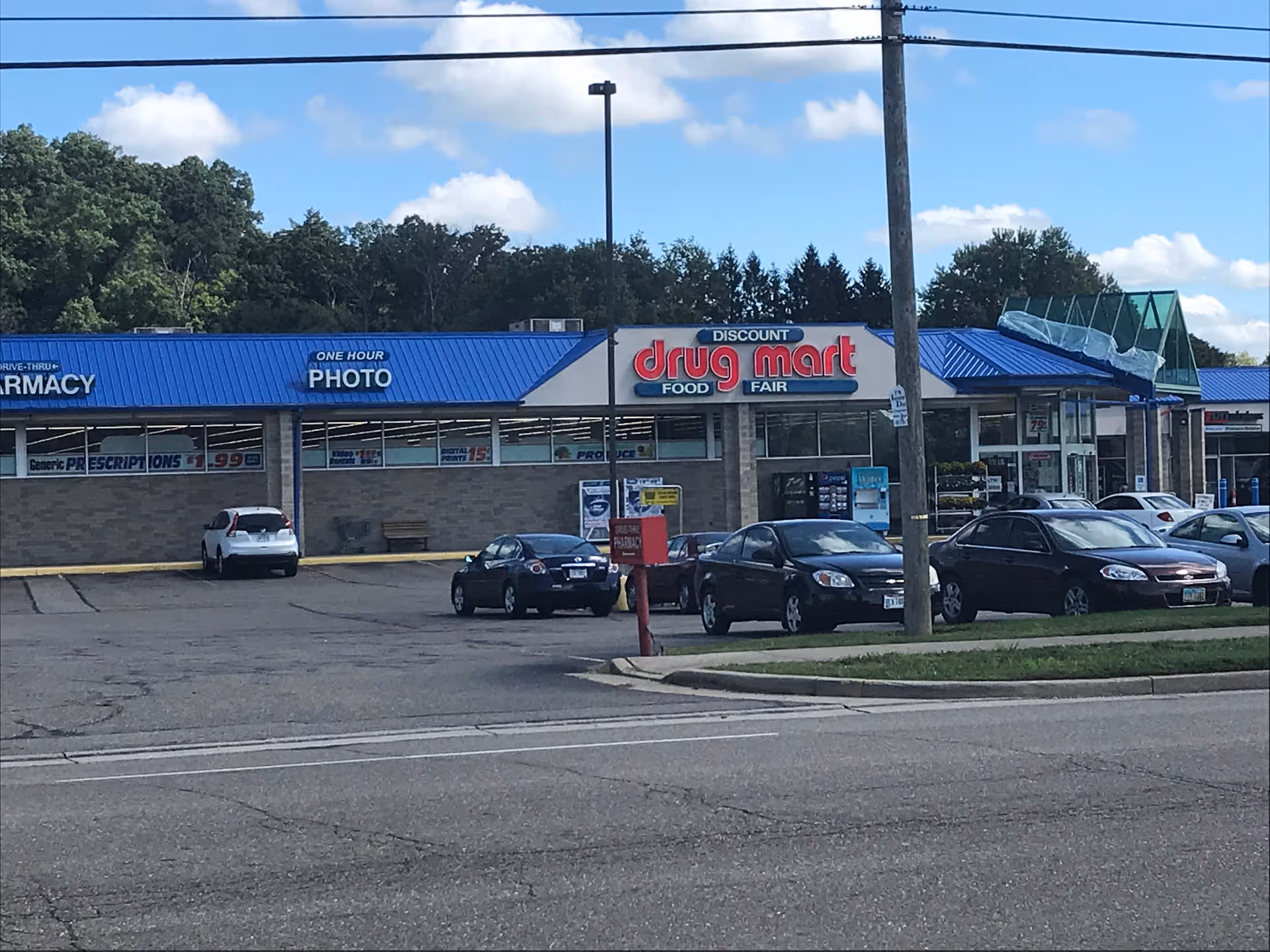 Exterior view of Discount Drug Mart storefront with blue awnings and parked cars.