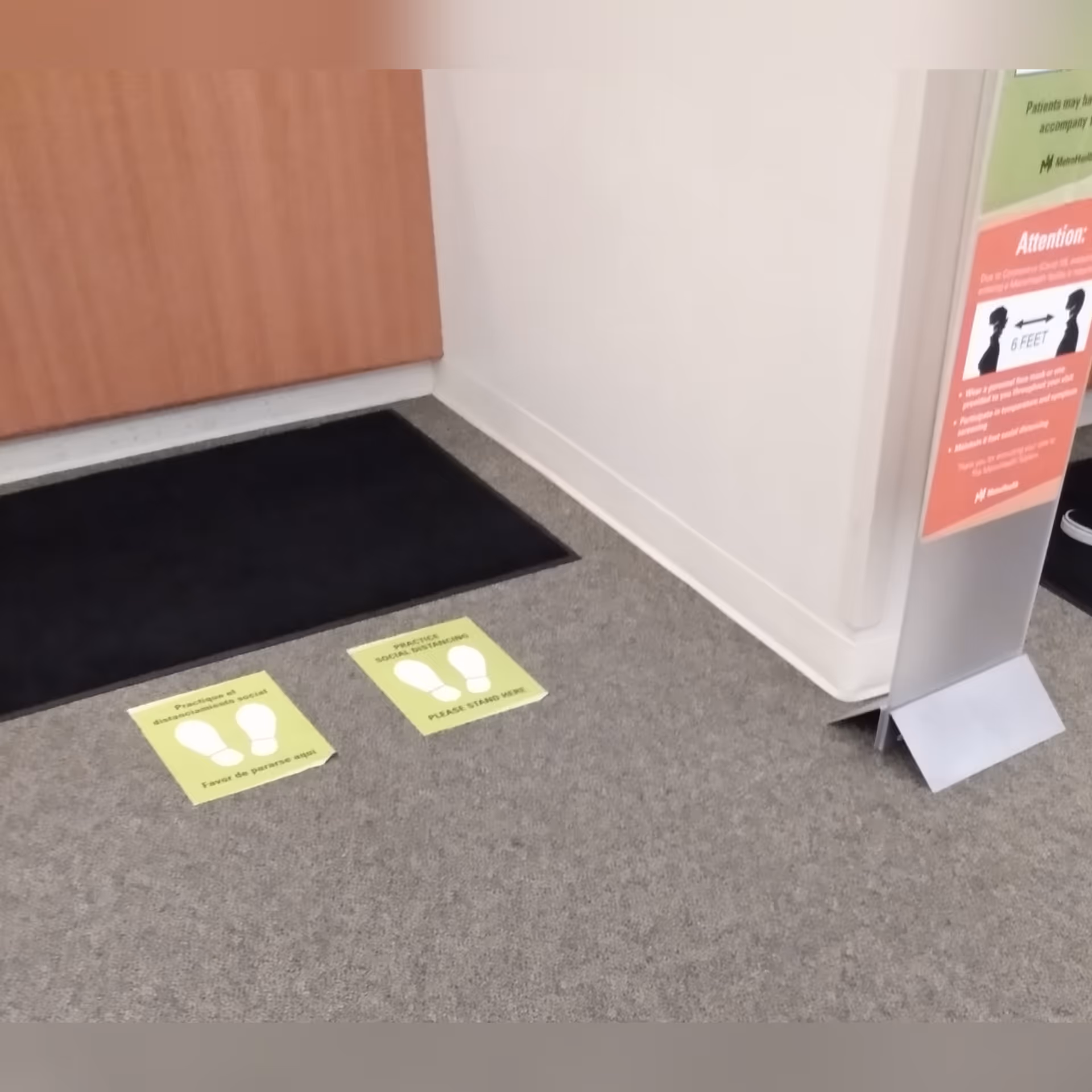 Interior facility entrance area with a black mat, yellow standing markers, and a sign.