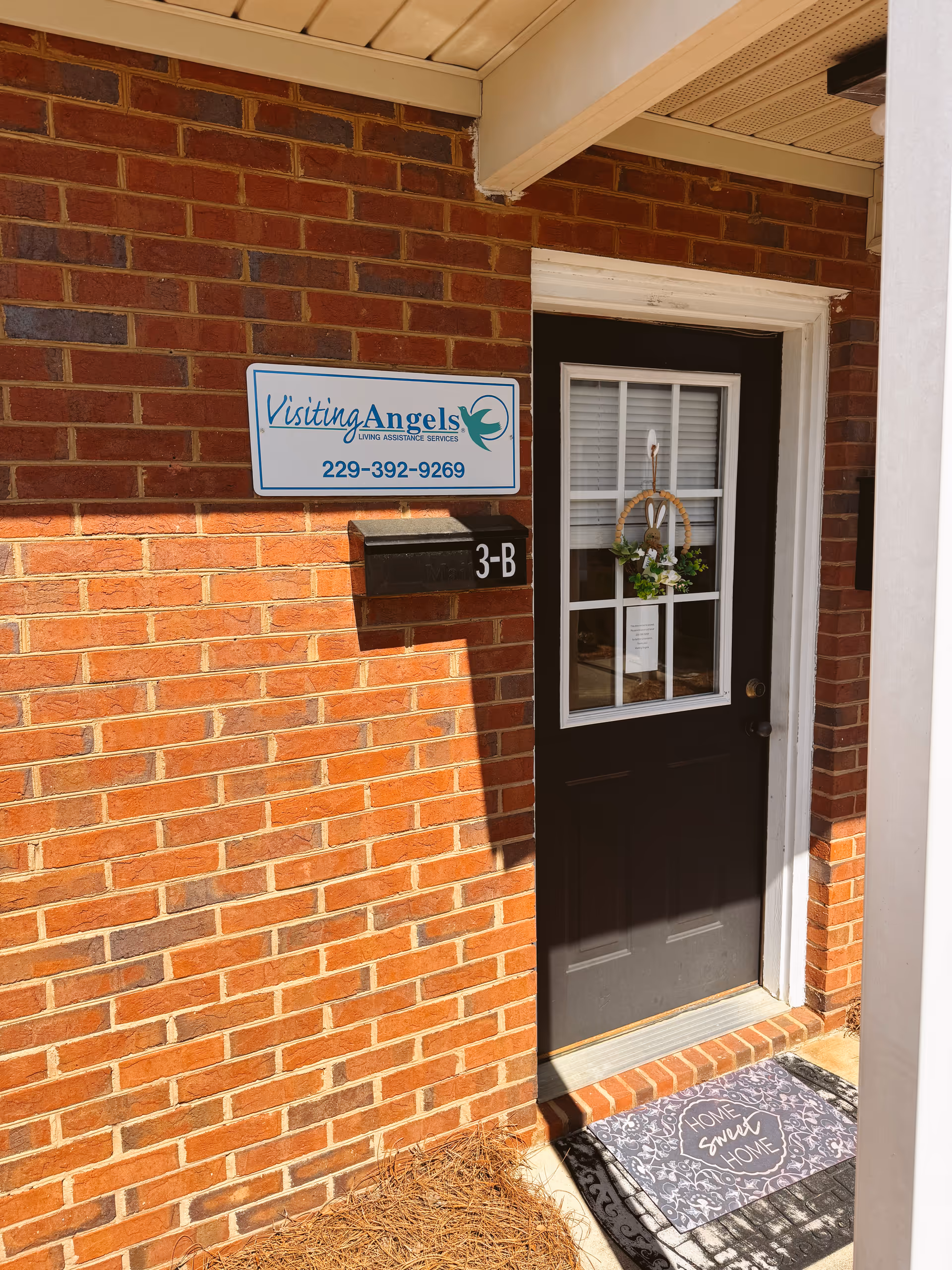 Brick exterior wall with Visiting Angels sign and front door with wreath.
