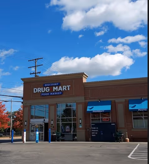 Brick Discount Drug Mart storefront with blue awnings and parking lot under a bright sky.