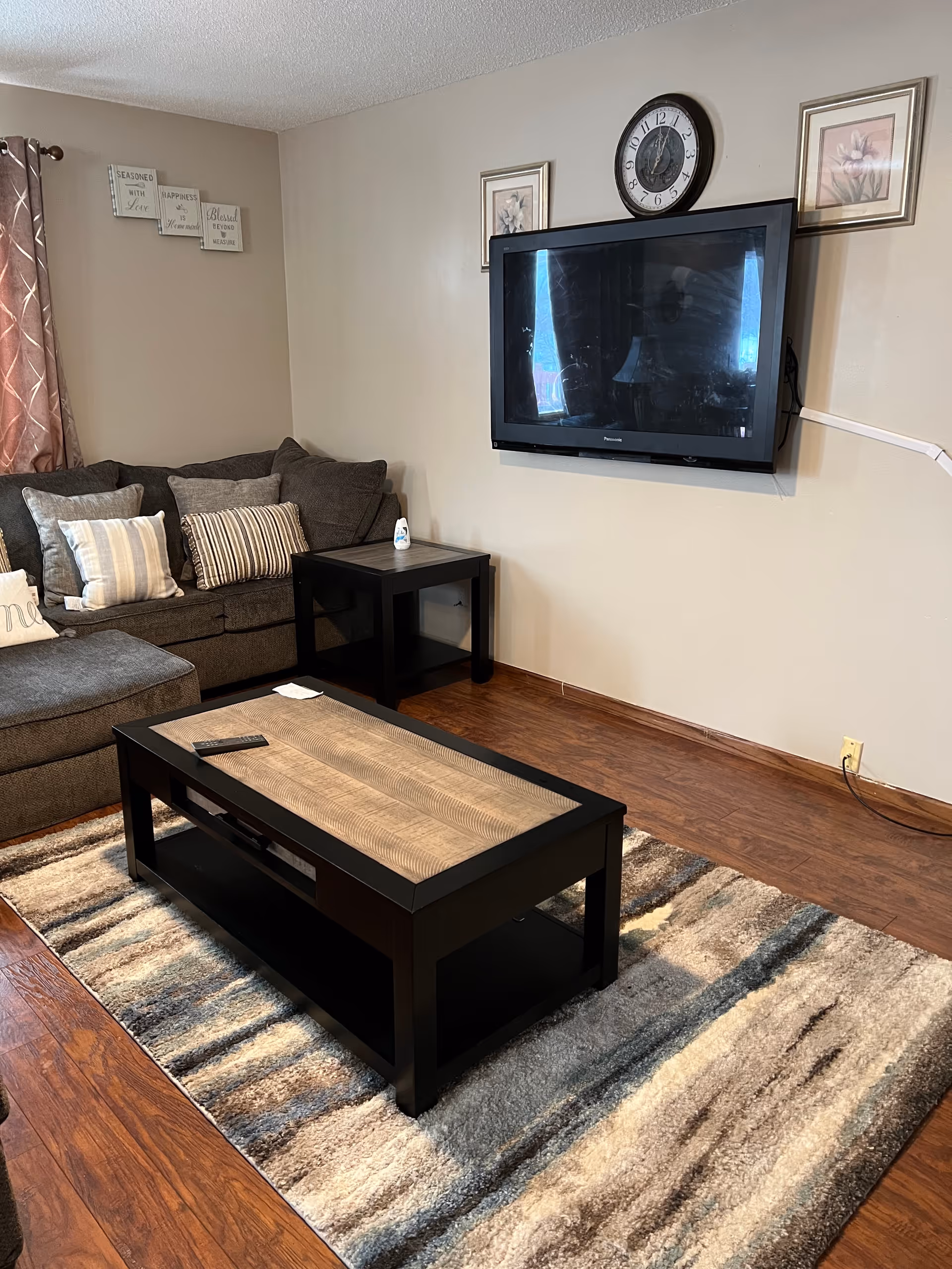 Cozy living room with a sectional sofa, coffee table, rug, and wall-mounted TV.
