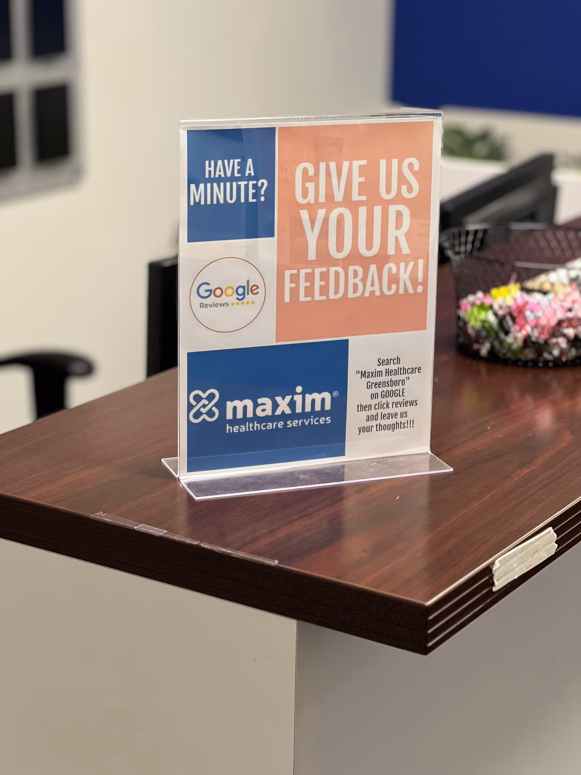 Reception desk with a feedback sign and Maxim Healthcare logo on a dark wood counter