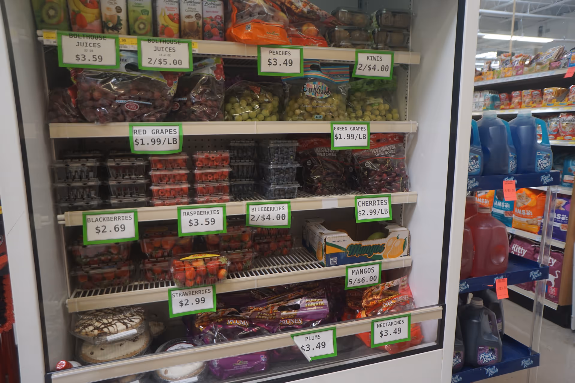 Open refrigerated display of fruits and berries with price tags at Discount Drug Mart.