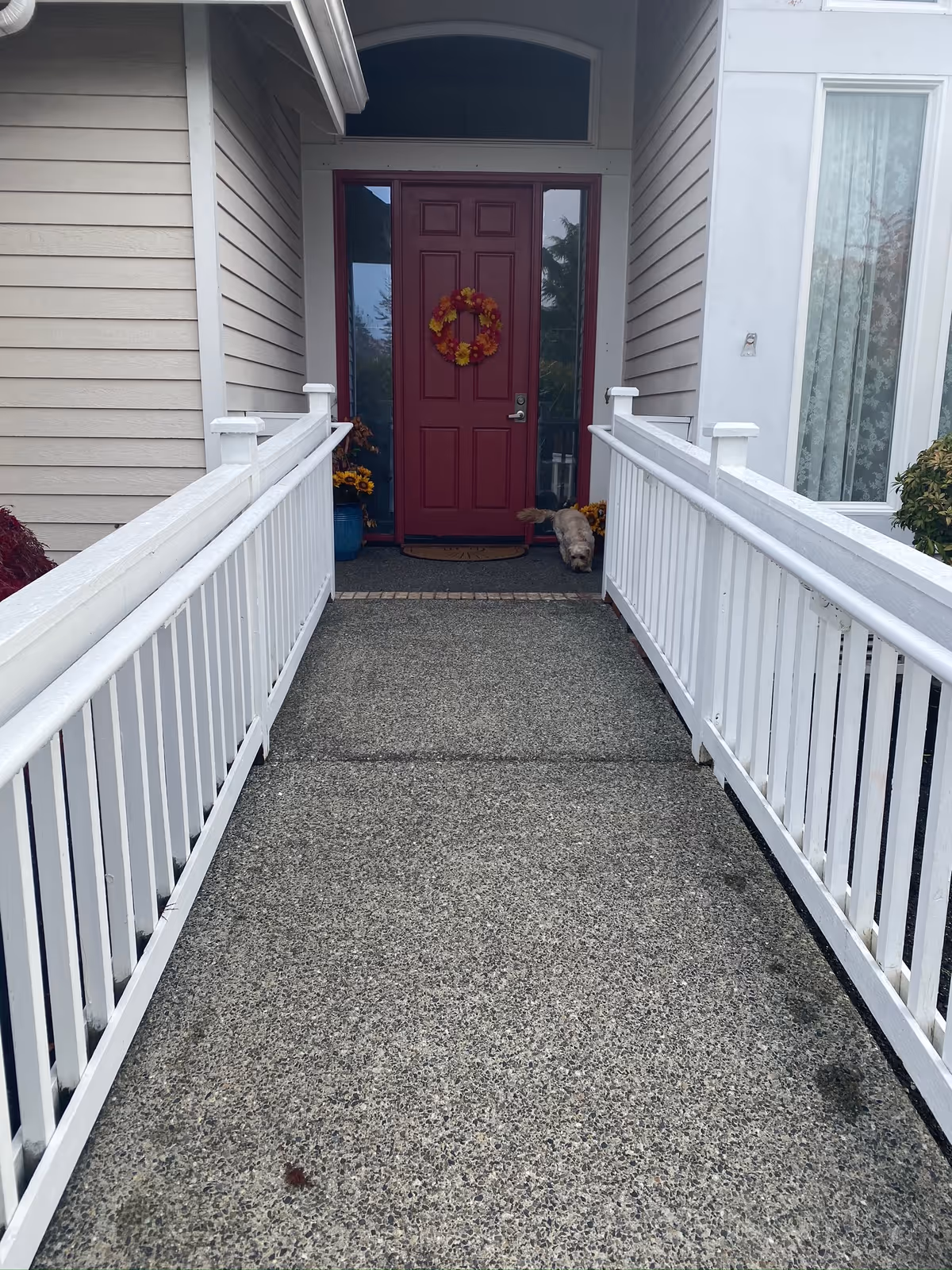 Front exterior walkway to a red door with a wreath and potted plants.