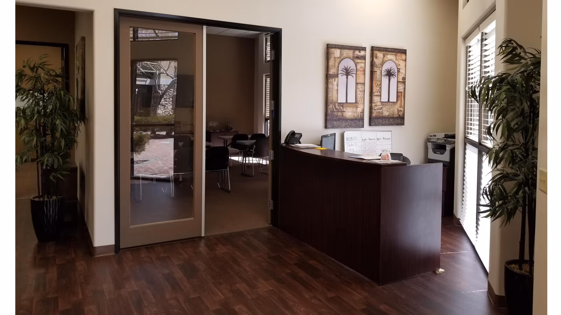 Reception desk in a modern senior living lobby with plants, glass door, and artwork.