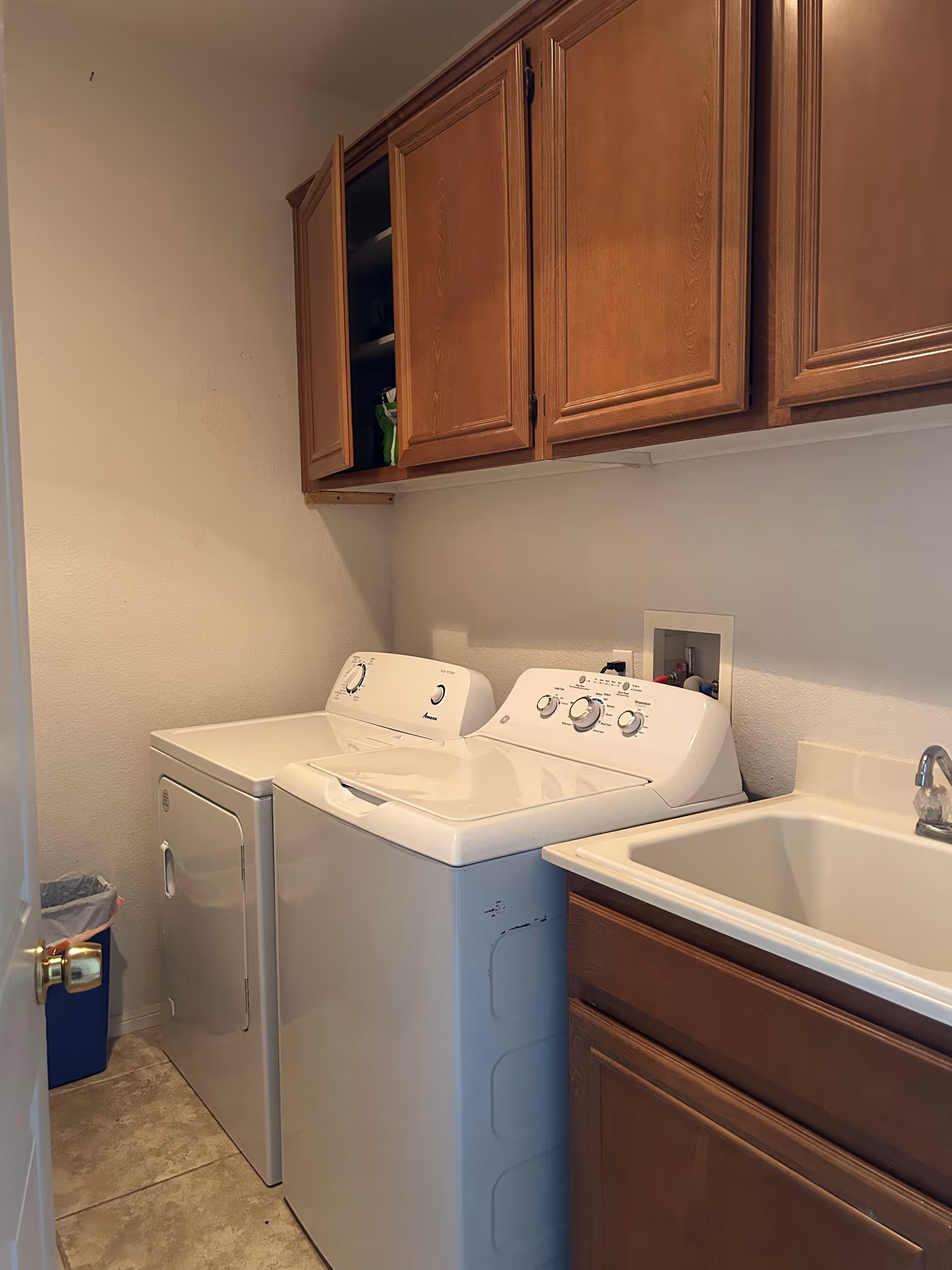 Laundry room with washer, dryer, sink, and wooden upper cabinets.