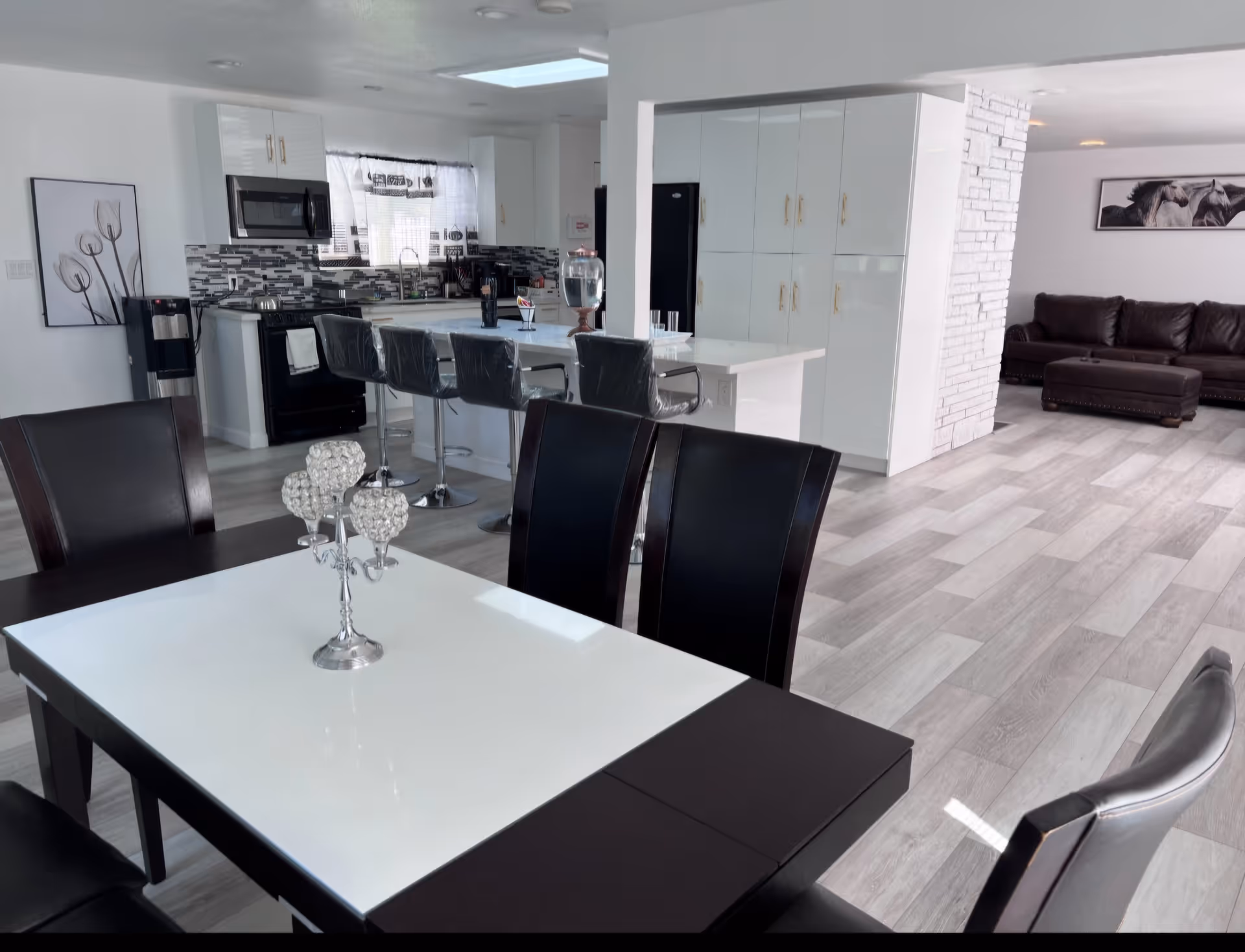 Open-concept dining, kitchen, and living area with white cabinetry and dark chairs.