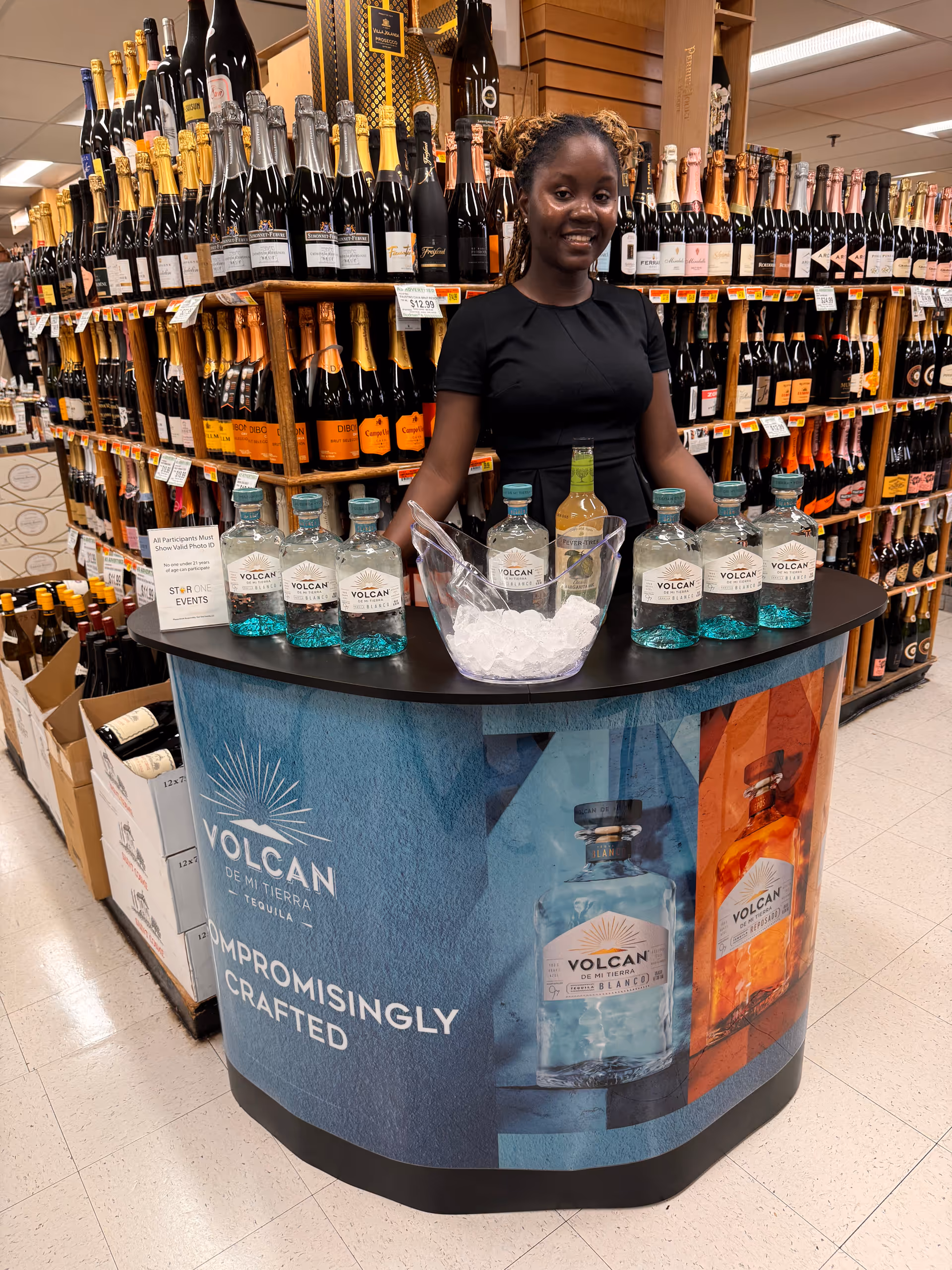 A woman stands behind a curved promotional liquor display in a store.