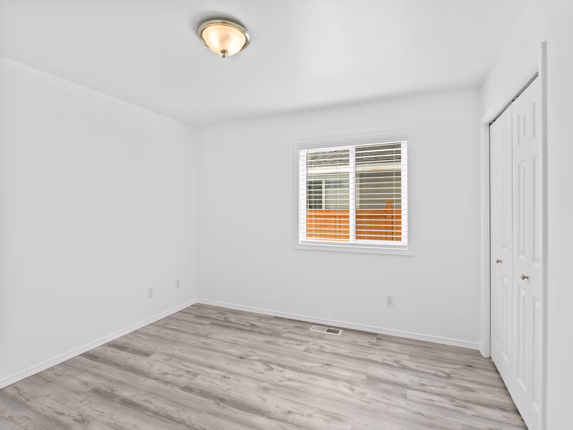 Bright empty room with white walls, a window, closet doors, and light wood flooring.