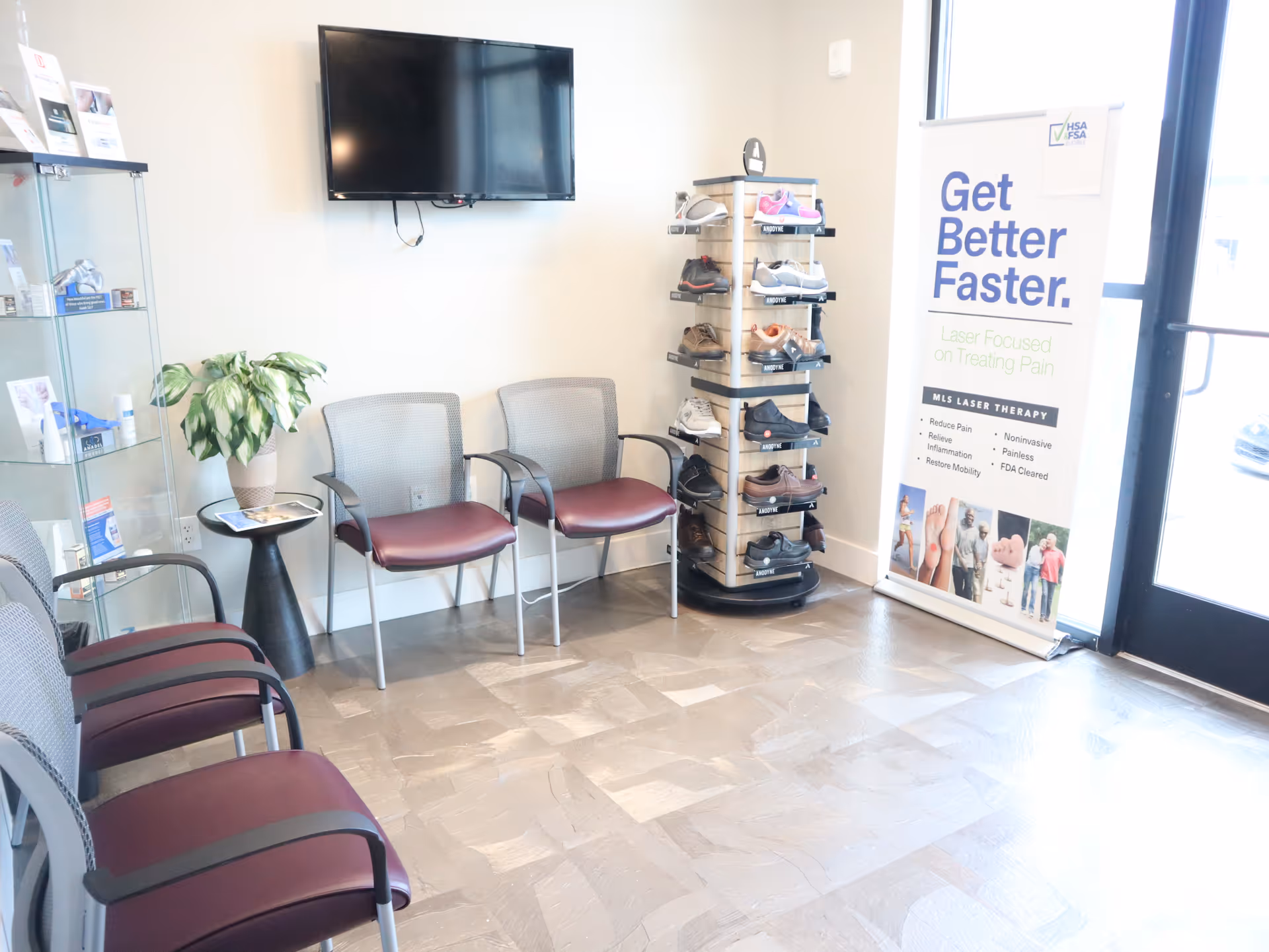 Waiting area with chairs, a wall-mounted TV, shoe display, plant, and promotional banner.