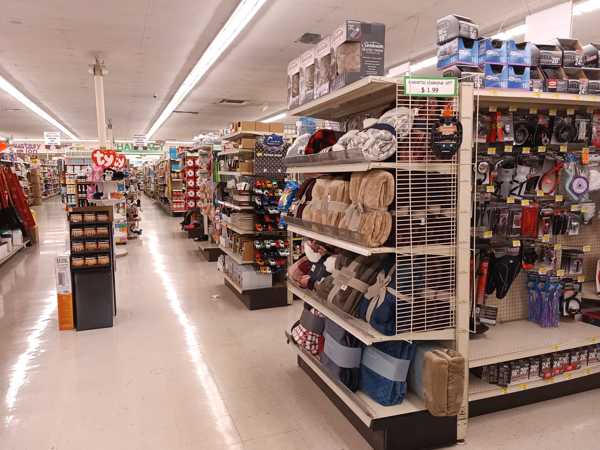 Wide aisle inside Discount Drug Mart featuring tall shelves of blankets and assorted goods.