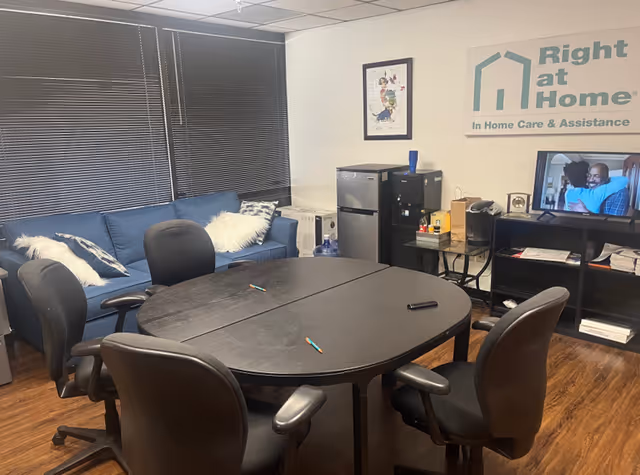 Office-style meeting room in a senior care facility with a round table, sofa, and TV.