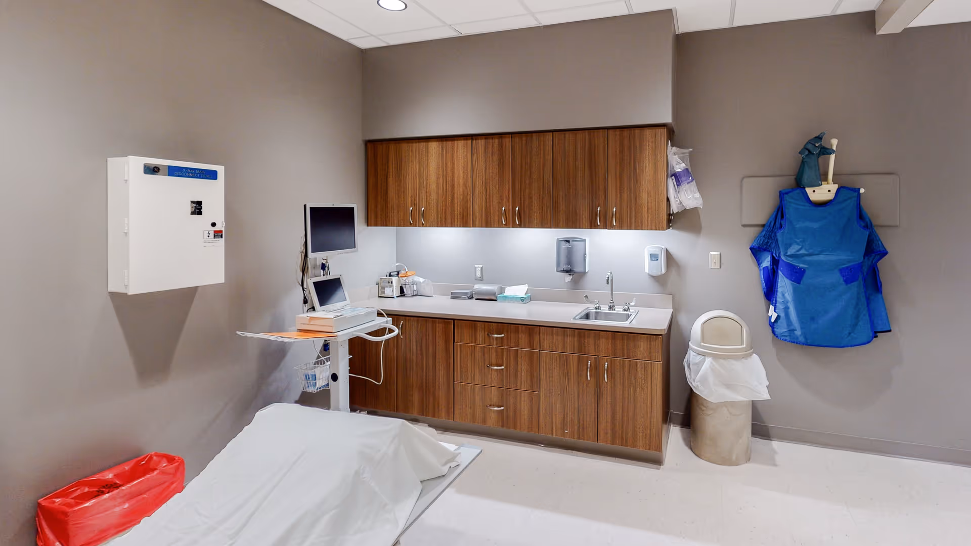Medical examination room with sink, countertops, cabinets, and a bed.