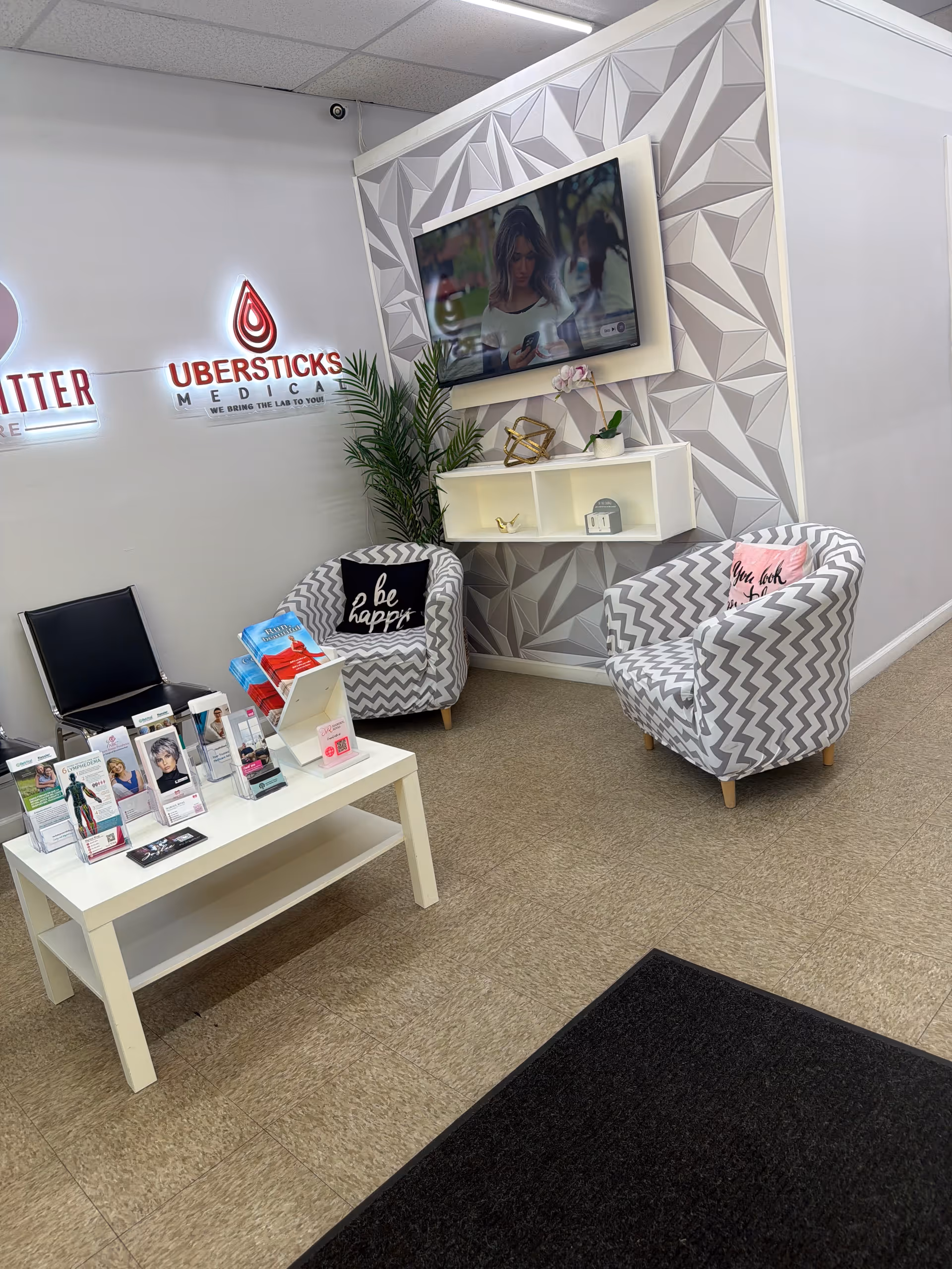 Reception seating area with chevron chairs, a wall TV, brochures on a table, branding signage.