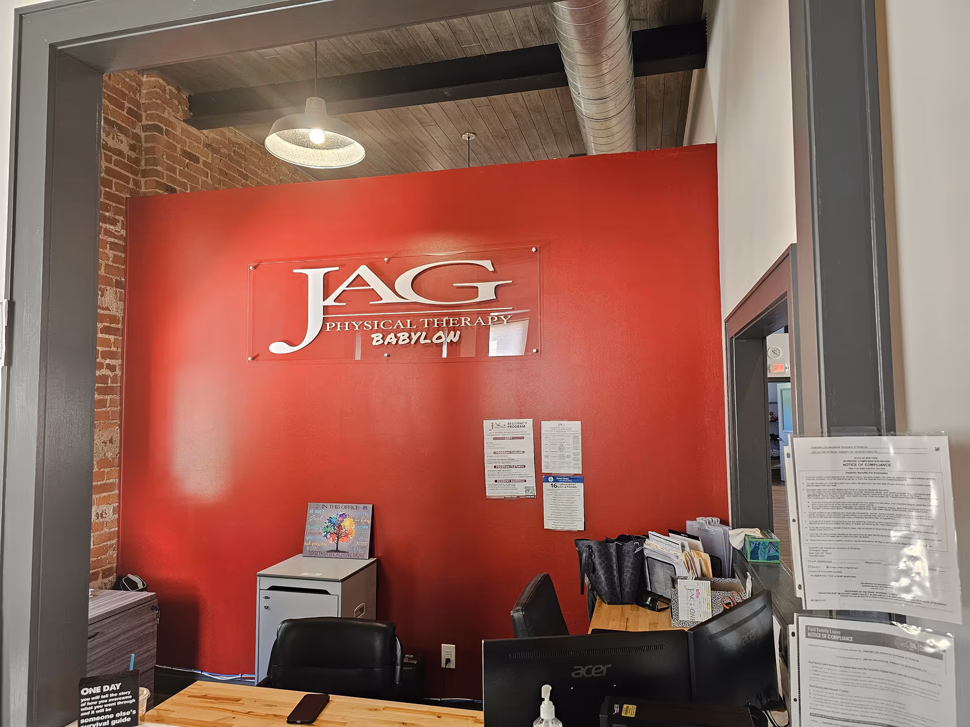 Red wall with JAG Physical Therapy sign, reception desk, and cluttered office space inside.