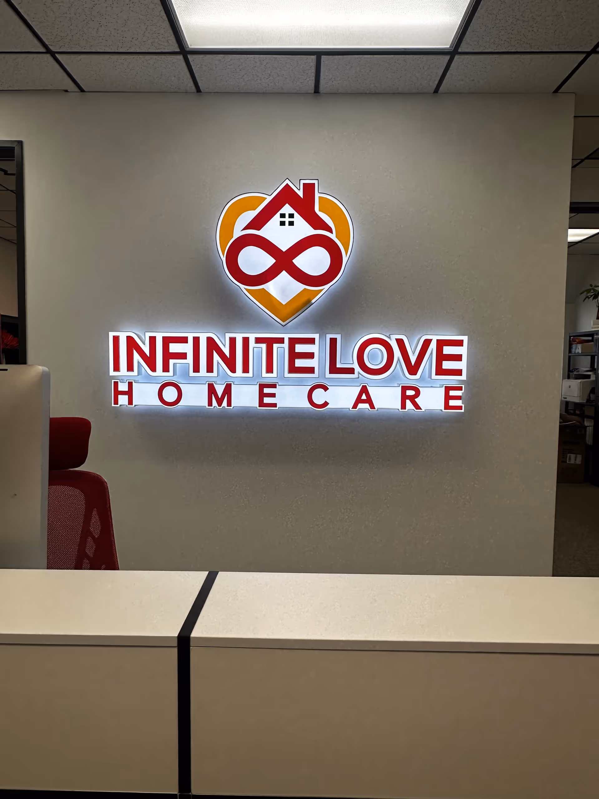 Reception area featuring illuminated Infinite Love Home Care logo on wall behind a white counter.