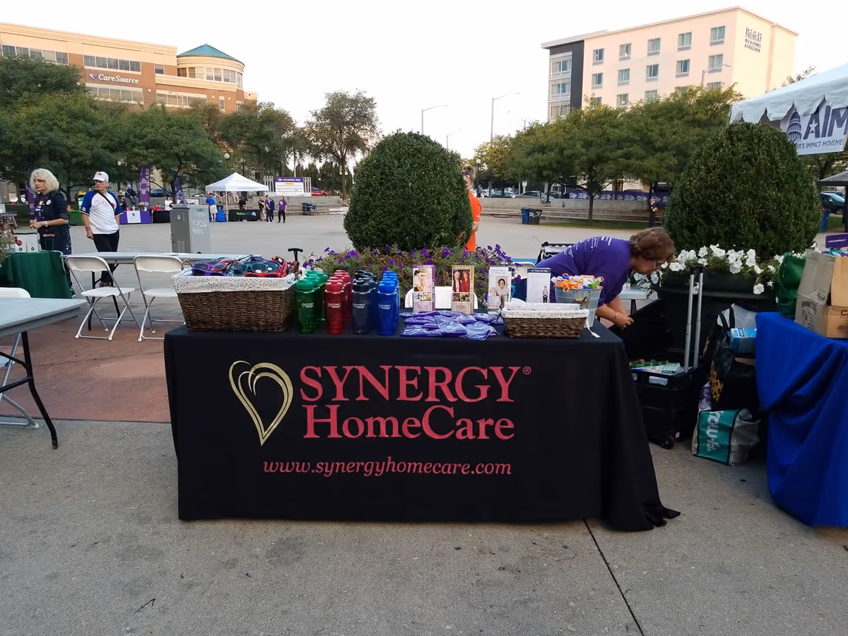 Outdoor Synergy HomeCare information table with staff and promotional items at a community event.