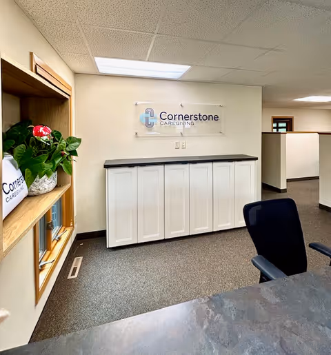 Reception area with Cornerstone Caregiving sign, white cabinets, plants, and a black office chair.