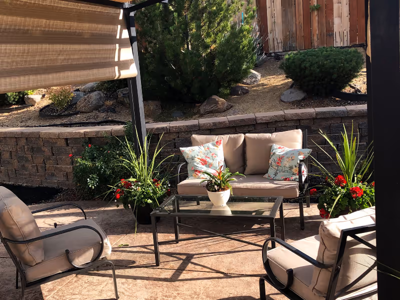 Outdoor patio with beige cushioned seating, glass table, and potted plants.