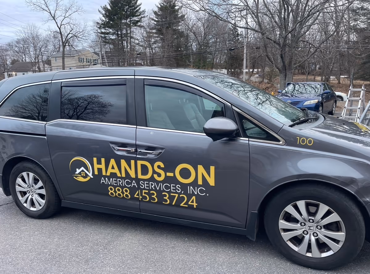 Grey Hands-On America Services van with yellow logo and phone number parked outdoors.