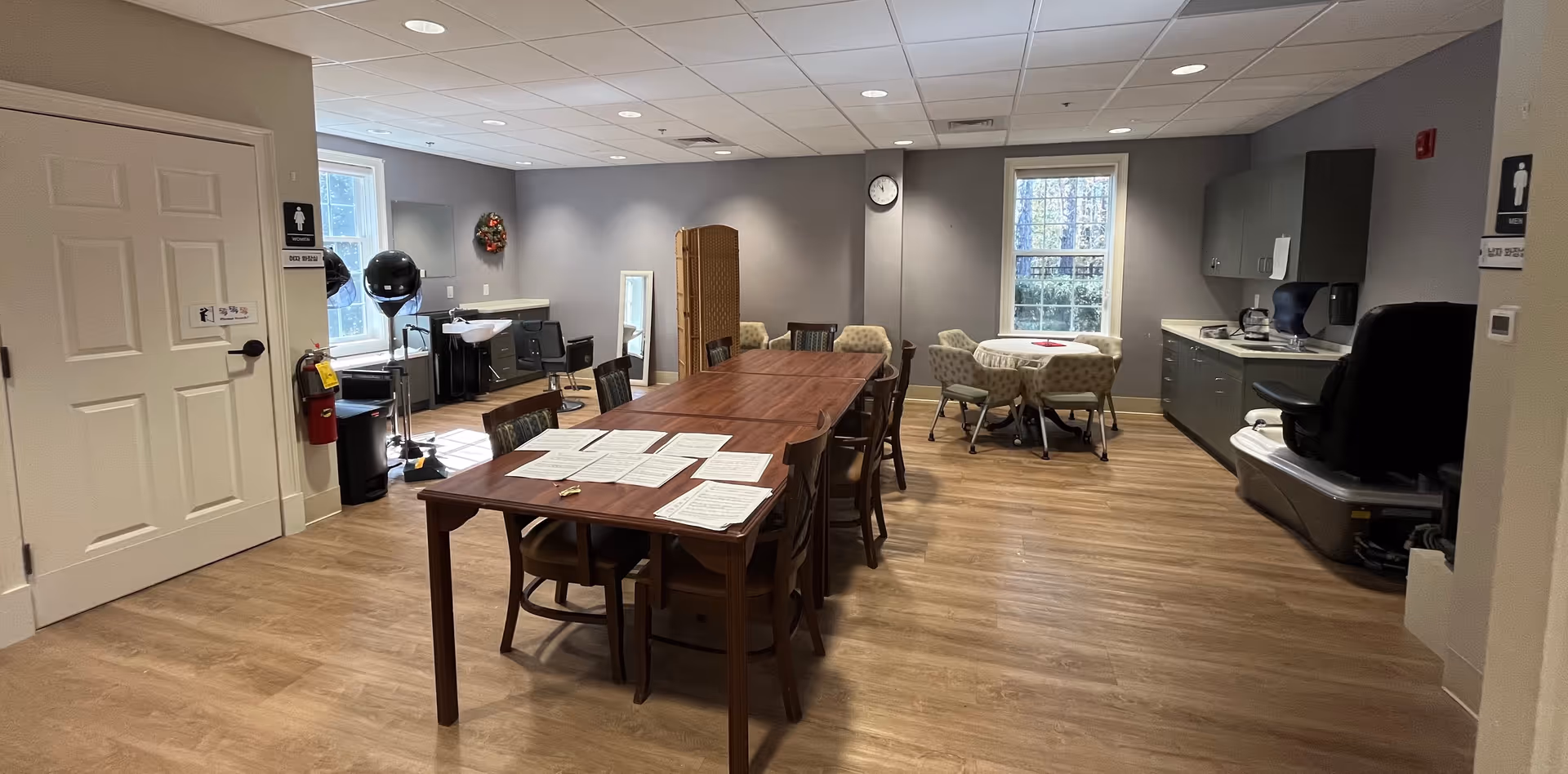 Spacious senior living common area with a long table, chairs, and a kitchenette.