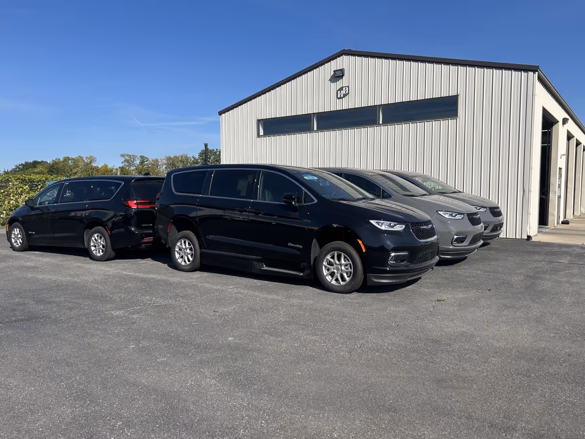 Several vans parked in front of a gray MobilityWorks building on a clear day.