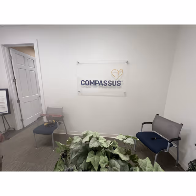 Interior waiting area with a Compassus sign, chairs, and plants.