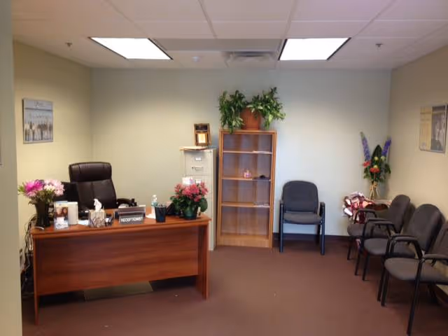Reception area with wooden desk, plants, and waiting chairs in a care facility