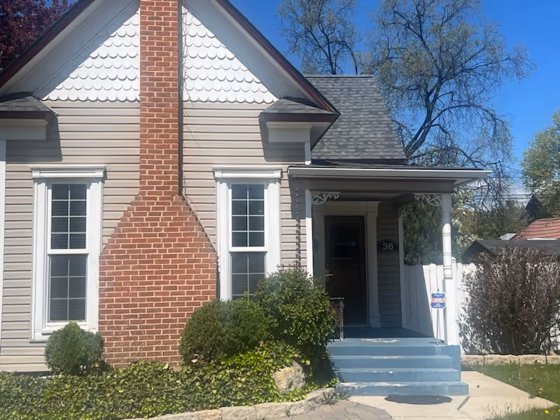 Front view of a beige house with a brick chimney, blue steps, and a small porch.