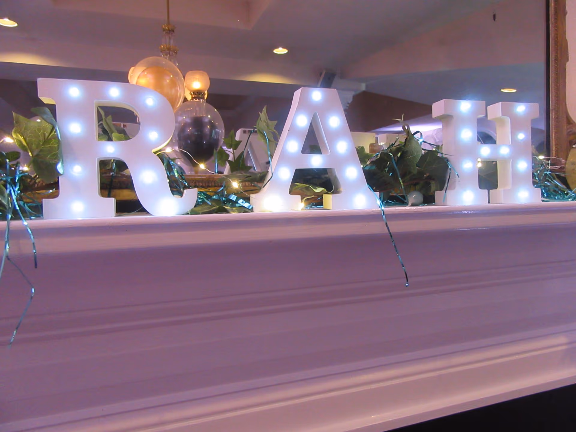 Illuminated 'RIGHT AT HOME' letters sit on a counter with greenery in a facility lobby.