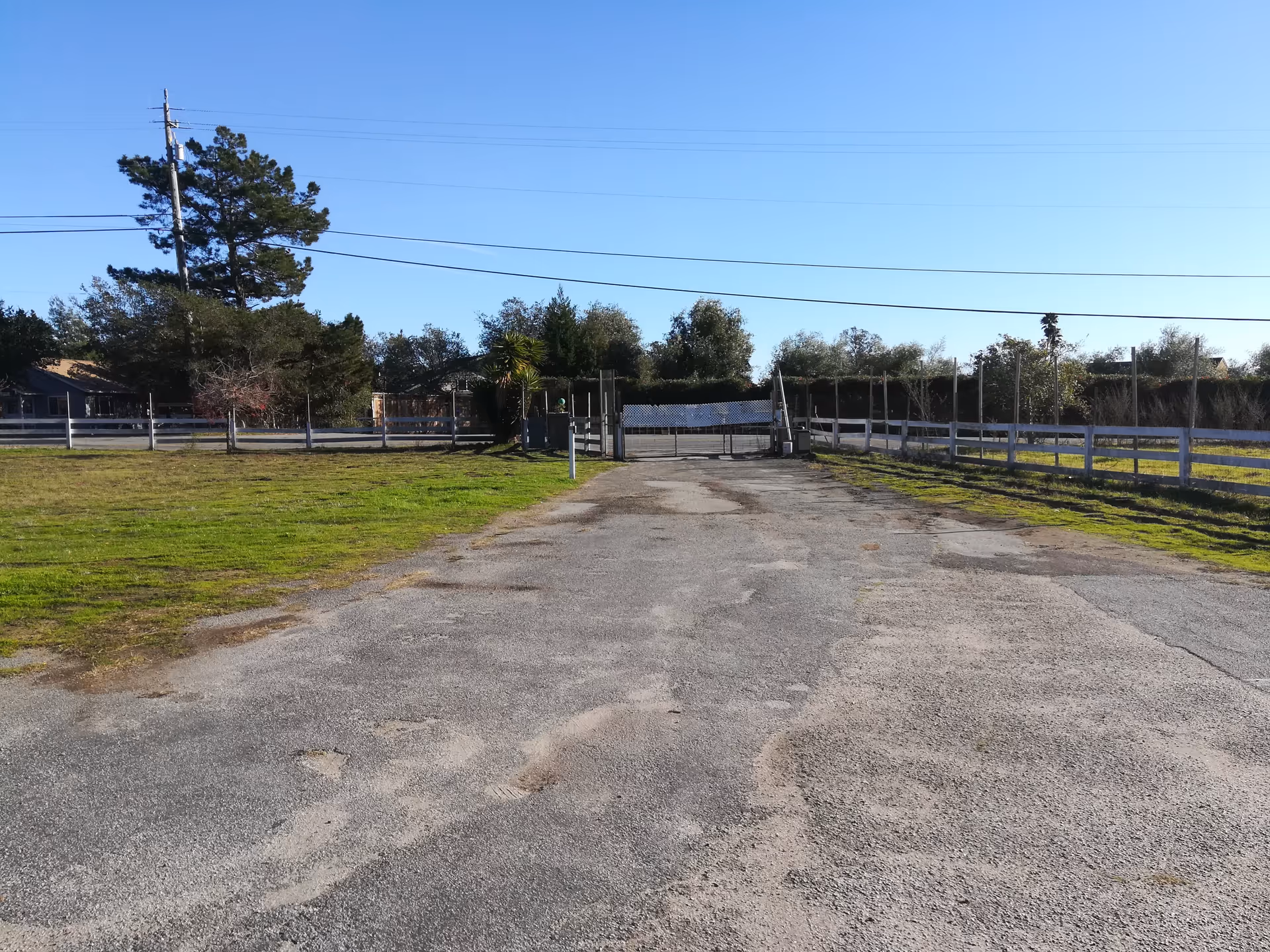 Long asphalt driveway leads to a gated facility entrance with fencing and open fields.