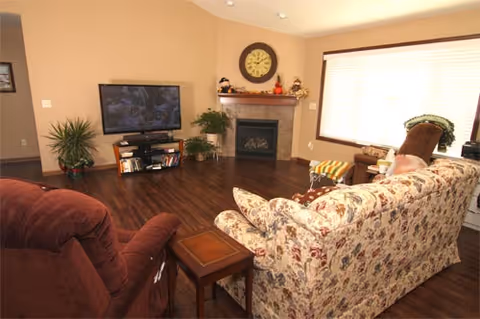 Cozy living room with floral sofa, burgundy chair, fireplace, and TV.