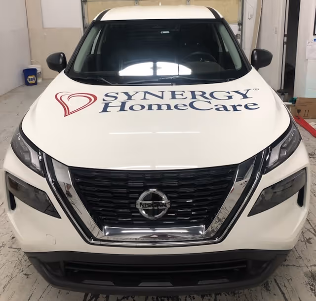 White SYNERGY HomeCare Nissan van inside a service bay at a facility.
