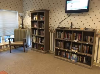 A quiet library lounge with bookshelves, a chair by a window, and a mounted TV.