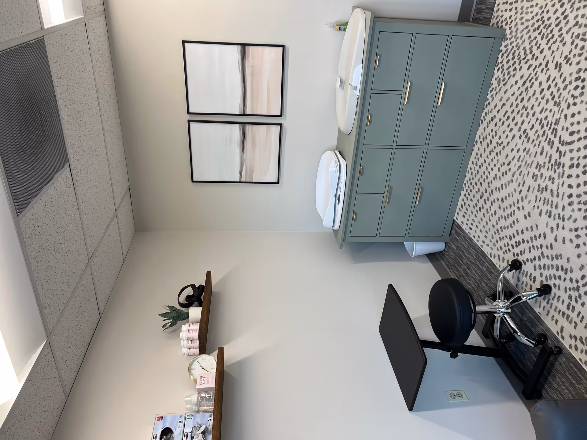 Lactation room with teal cabinet, dual sinks, chair, and patterned carpet.