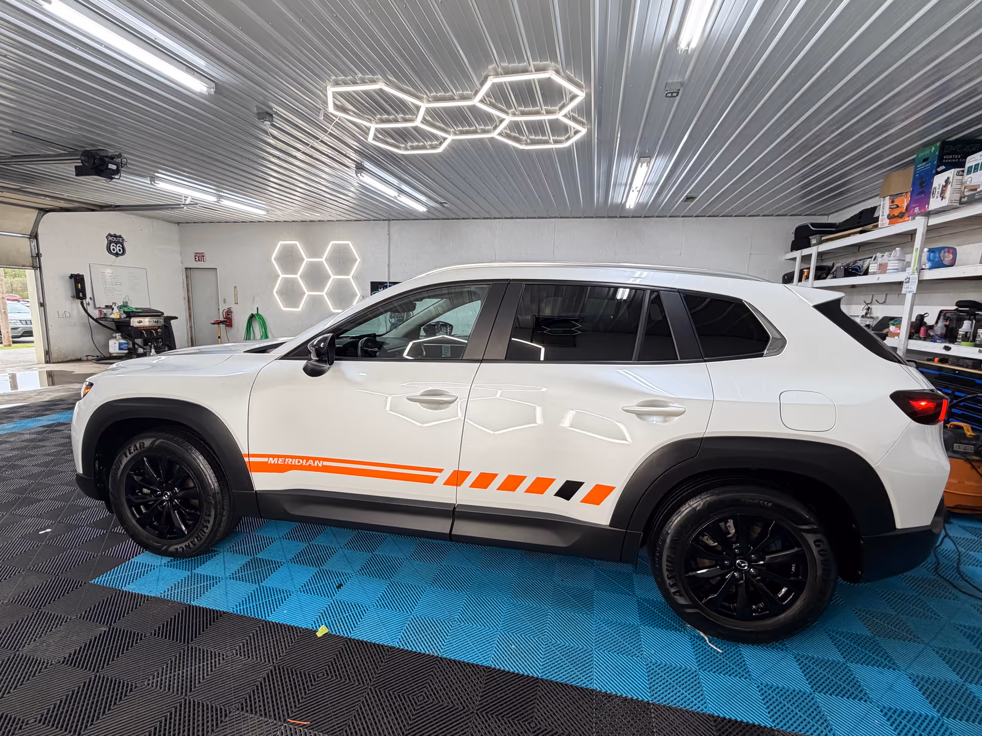 White SUV with orange stripes parked inside a brightly lit garage with hexagonal ceiling lights.