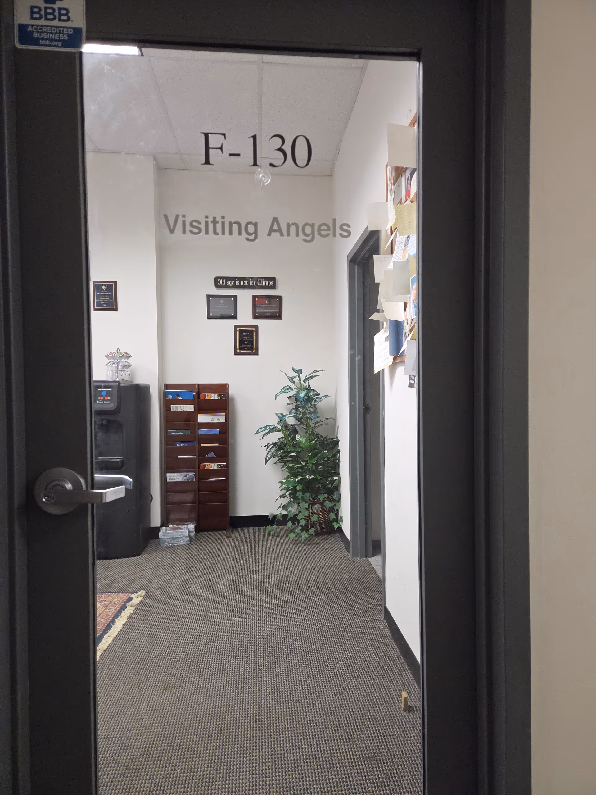 Interior hallway with a glass door reading F-130 Visiting Angels, plus a plant and mail rack.