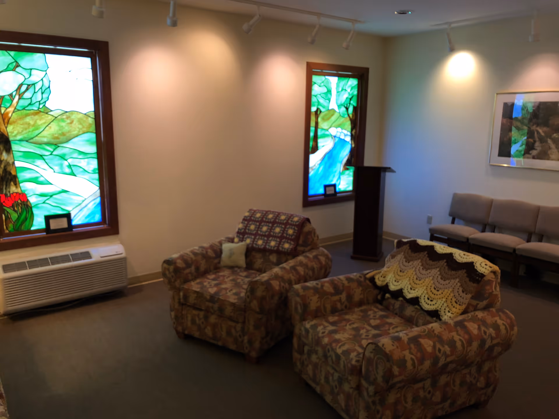 Cozy living room with floral armchairs, stained glass windows, and beige chairs.
