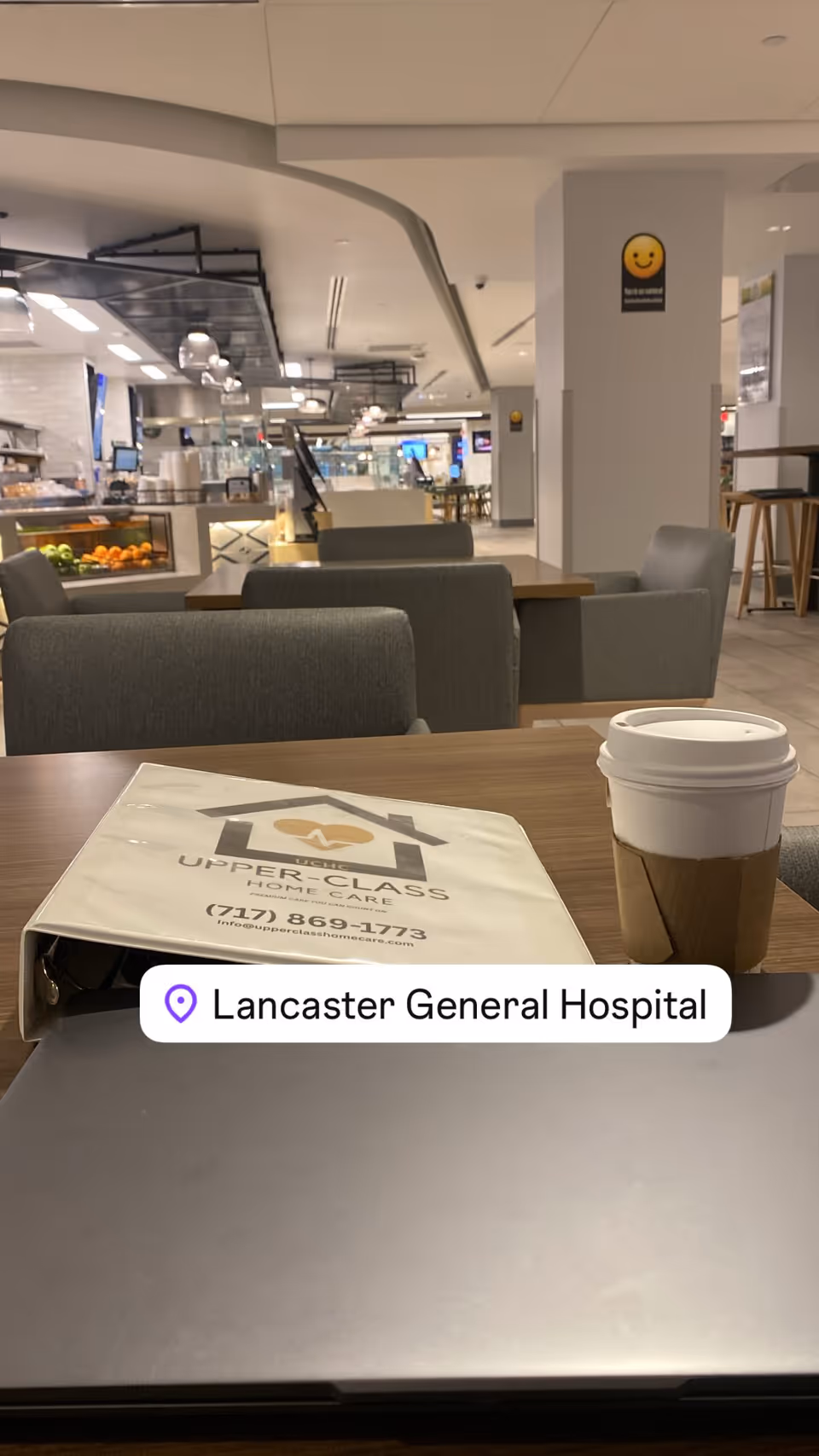 Table with Upper-Class Home Care brochure and takeout coffee cup in a modern cafe.