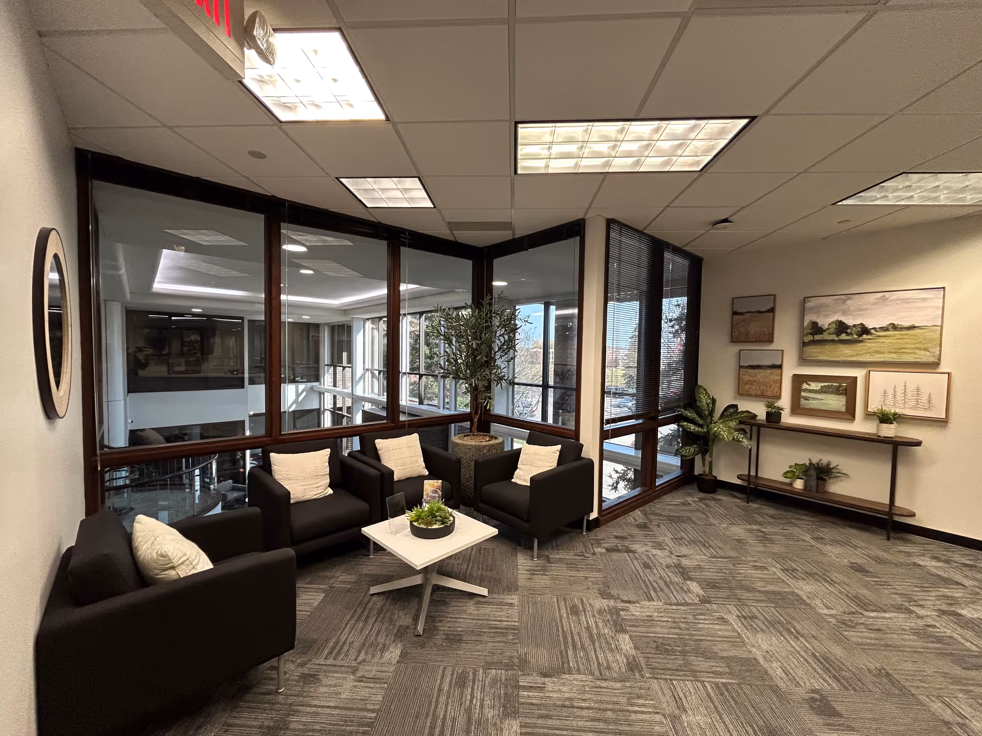 A contemporary lounge area with black armchairs, a white coffee table, plants, and large windows.