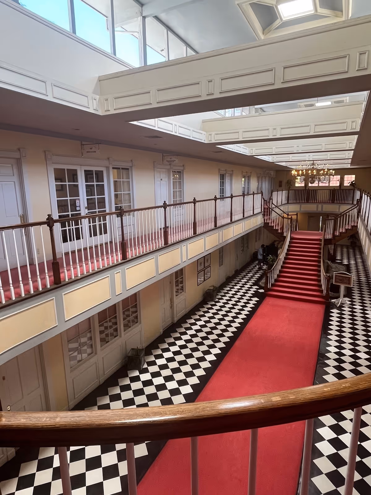 Indoor corridor with red carpet and checkered floor, balconies along the upper level.